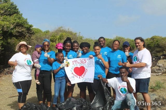 一群志愿者围着“195in365 Earth Day ’24 Make a Change, Grenada”标牌竖起大拇指，他们大多身穿蓝色T恤、戴着劳动手套，旁边是装满的垃圾袋。